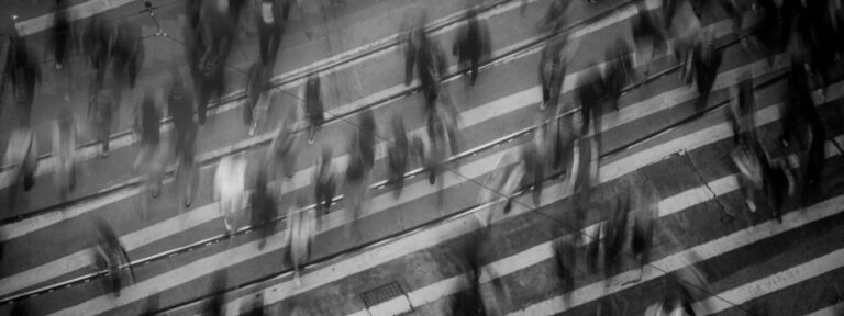 Blurred pedestrians crossing a busy street.