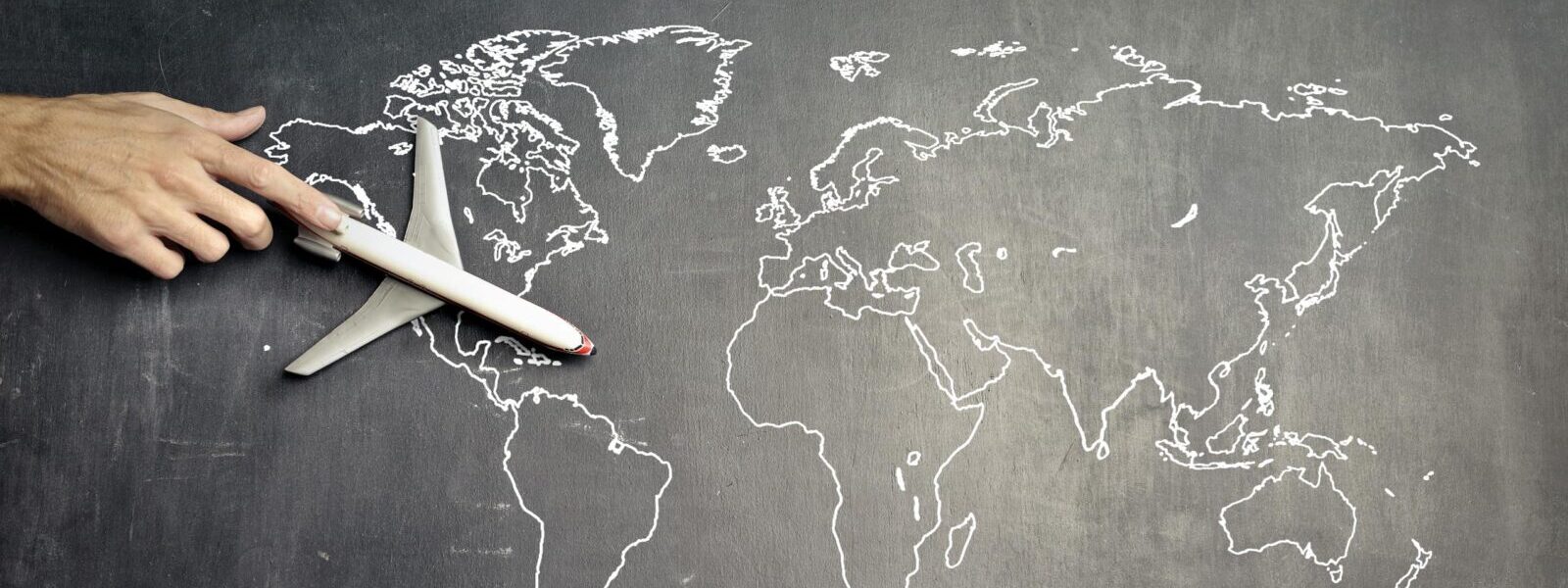 From above of crop anonymous person driving toy airplane on empty world map.